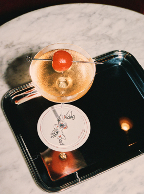 Cocktail mousseux en coupe fine sur table en marbre, lampe et carte de cocktails en fond &ndash; Cherry Saint-Tropez